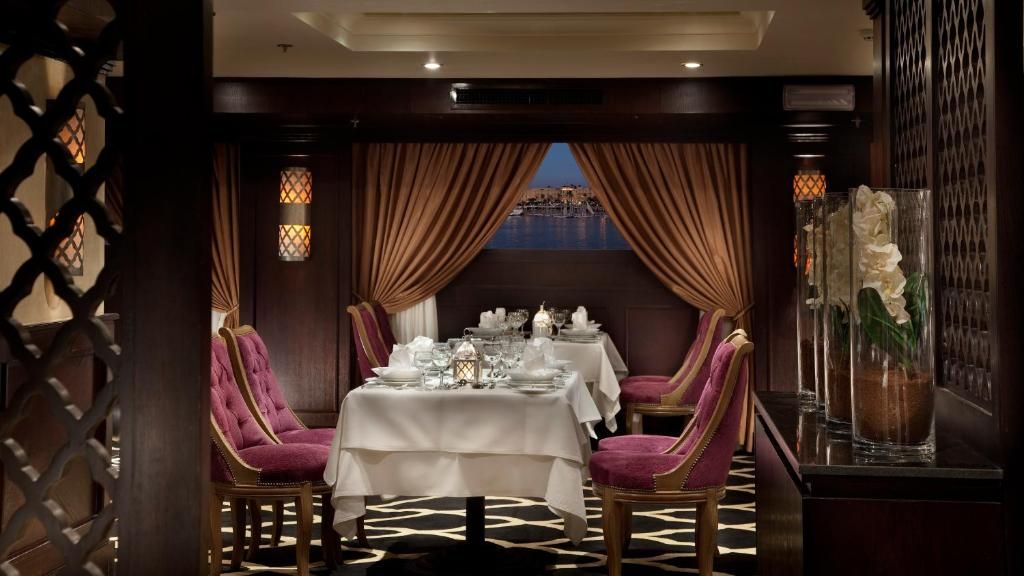 A dining area with a table set for two, a view of the sea, and a decorative vase with flowers.