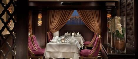 A dining area with a table set for two, a view of the sea, and a decorative vase with flowers.