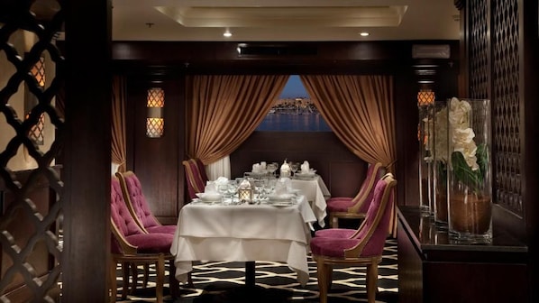 Un coin repas avec une table dressée pour deux personnes, une vue sur la mer et un vase décoratif rempli de fleurs.