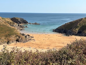 Une plage côtière bordée de falaises rocheuses, avec une mer d’un bleu limpide et un rivage sablonneux.