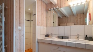 Un baño moderno con paneles de madera, dos lavamanos, un espejo grande y cabina de ducha a ras de suelo.