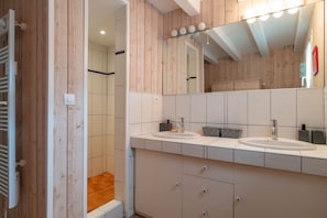 Une salle de bain moderne avec un lambris en bois, deux vasques, un grand miroir et une douche à l’italienne.