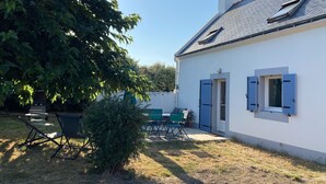 Una casa blanca con contraventanas azules, un pequeño jardín y un patio con mobiliario exterior.