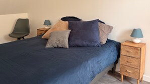 A bed with a blue bedspread, multiple pillows, two bedside tables with lamps, and a chair.