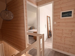 A wooden interior with a staircase, a bed with a patterned bedspread, a mirror, and a hanging light fixture. - Ty Eurvad - Proche des plages (Bangor)