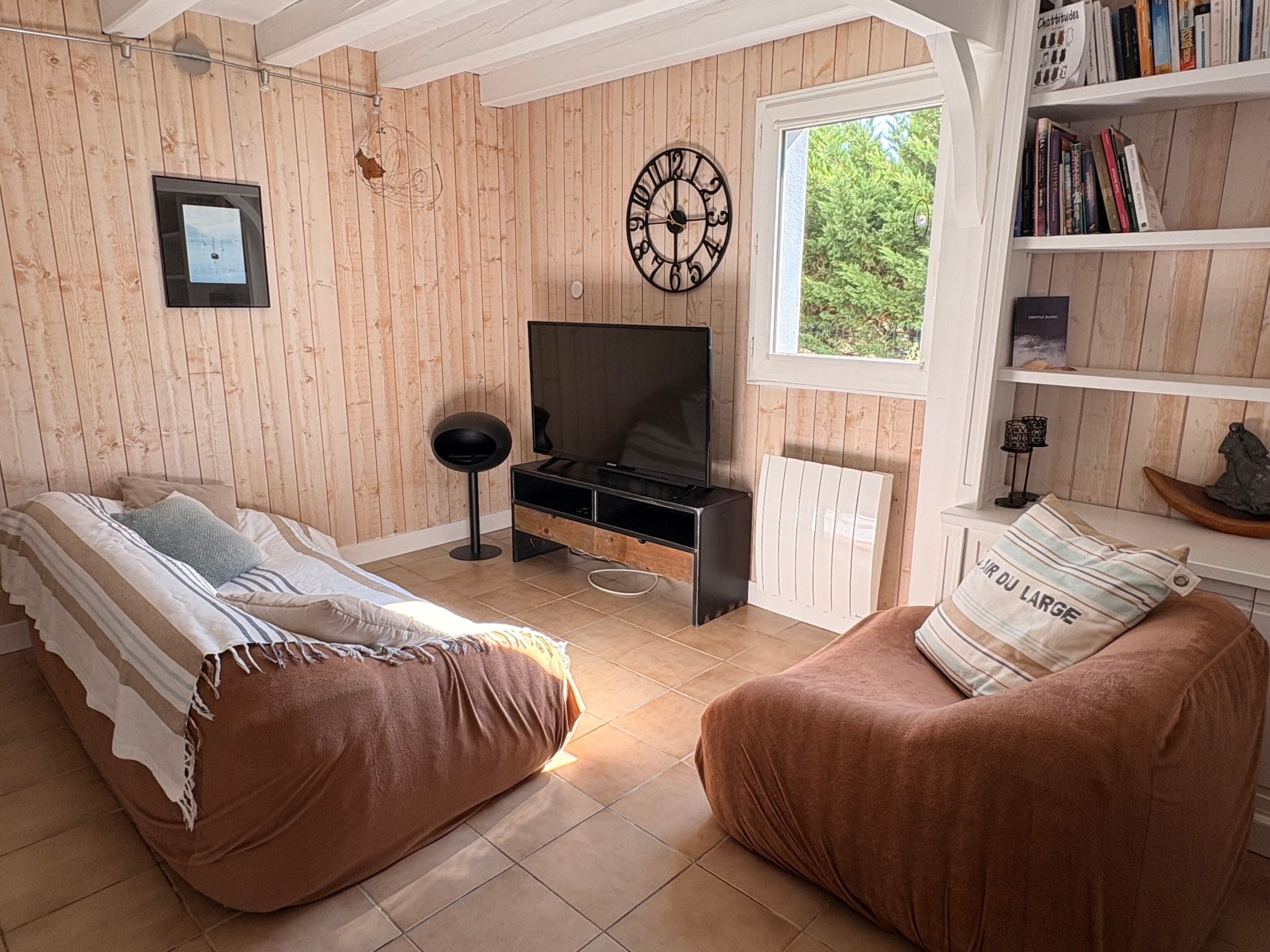 Una habitación con cama, sofá, televisión, estantería y ventana con vistas a zonas verdes.