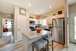 Una cocina moderna con armarios blancos, un refrigerador de acero inoxidable, una encimera de granito y un reloj en la pared.