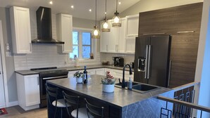 A modern kitchen with a central island, bar stools, stainless steel appliances, and pendant lighting.