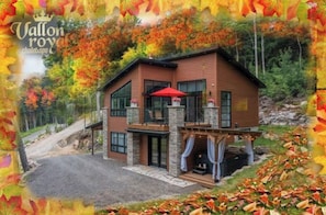 Une maison en bois à deux étages, avec des fondations en pierre, un parapluie rouge et une cheminée.