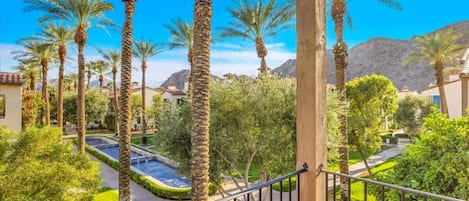 A balcony with a view of a landscaped garden, palm trees, and a mountain in the background.