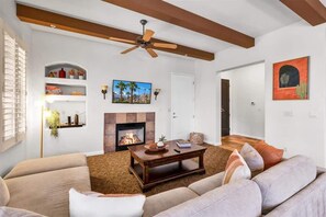 Una sala de estar con chimenea, ventilador de techo y un cuadro grande en la pared.