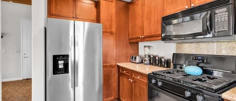 A kitchen with wooden cabinets, a stainless steel refrigerator, a microwave, a stove, and a toaster.