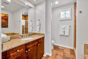 A bathroom with a granite countertop sink, wooden vanity, and a large mirror. There are towels hanging on the wall and a window with a decorative grille.