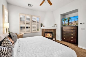 A bedroom with a large bed, a fireplace, a TV, and a dresser.