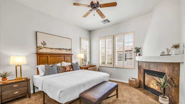 A bedroom with a bed, a bench, a fireplace, and a ceiling fan.