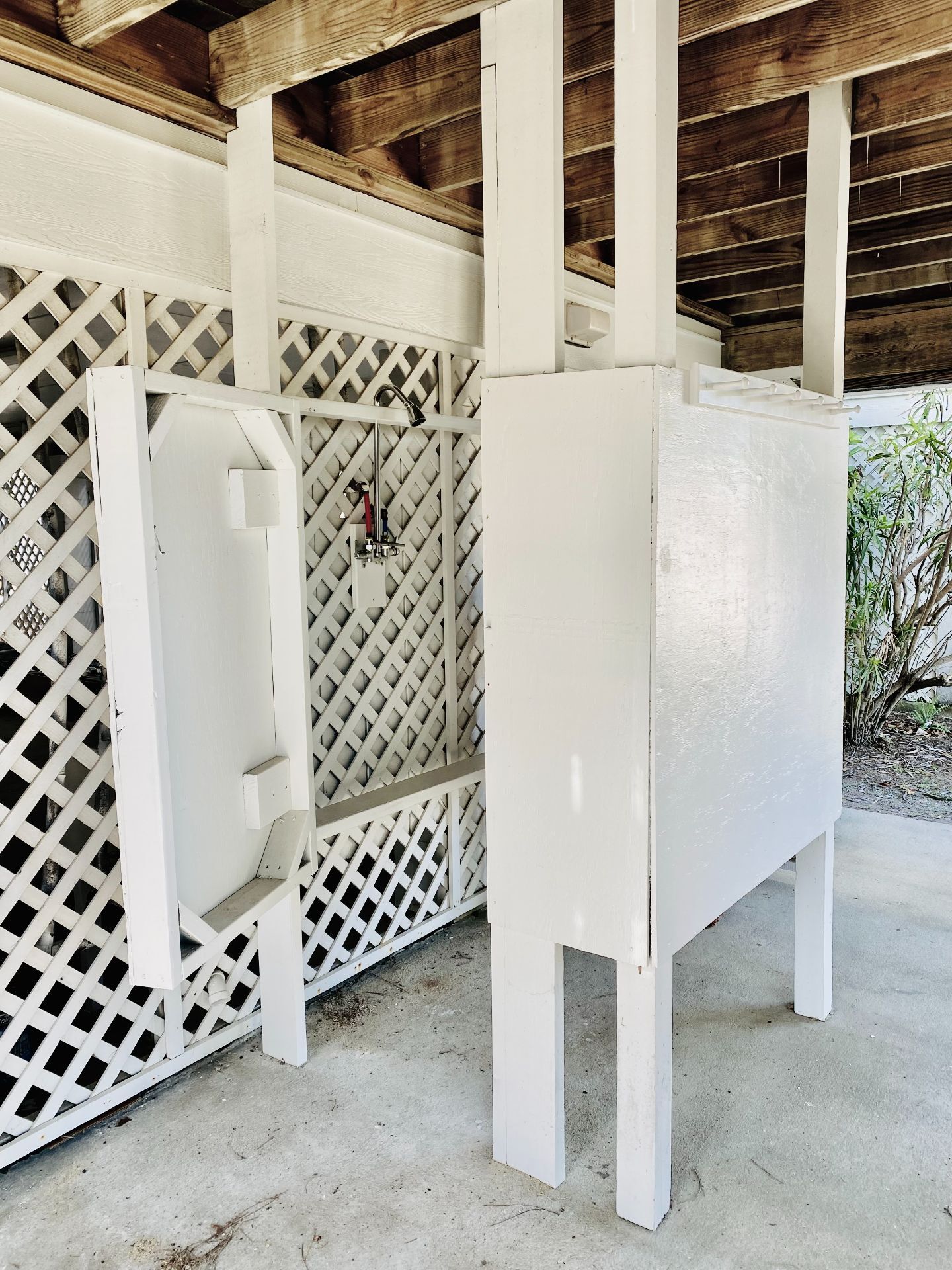 A white, enclosed outdoor shower area with a wooden ceiling and a lattice wall.
