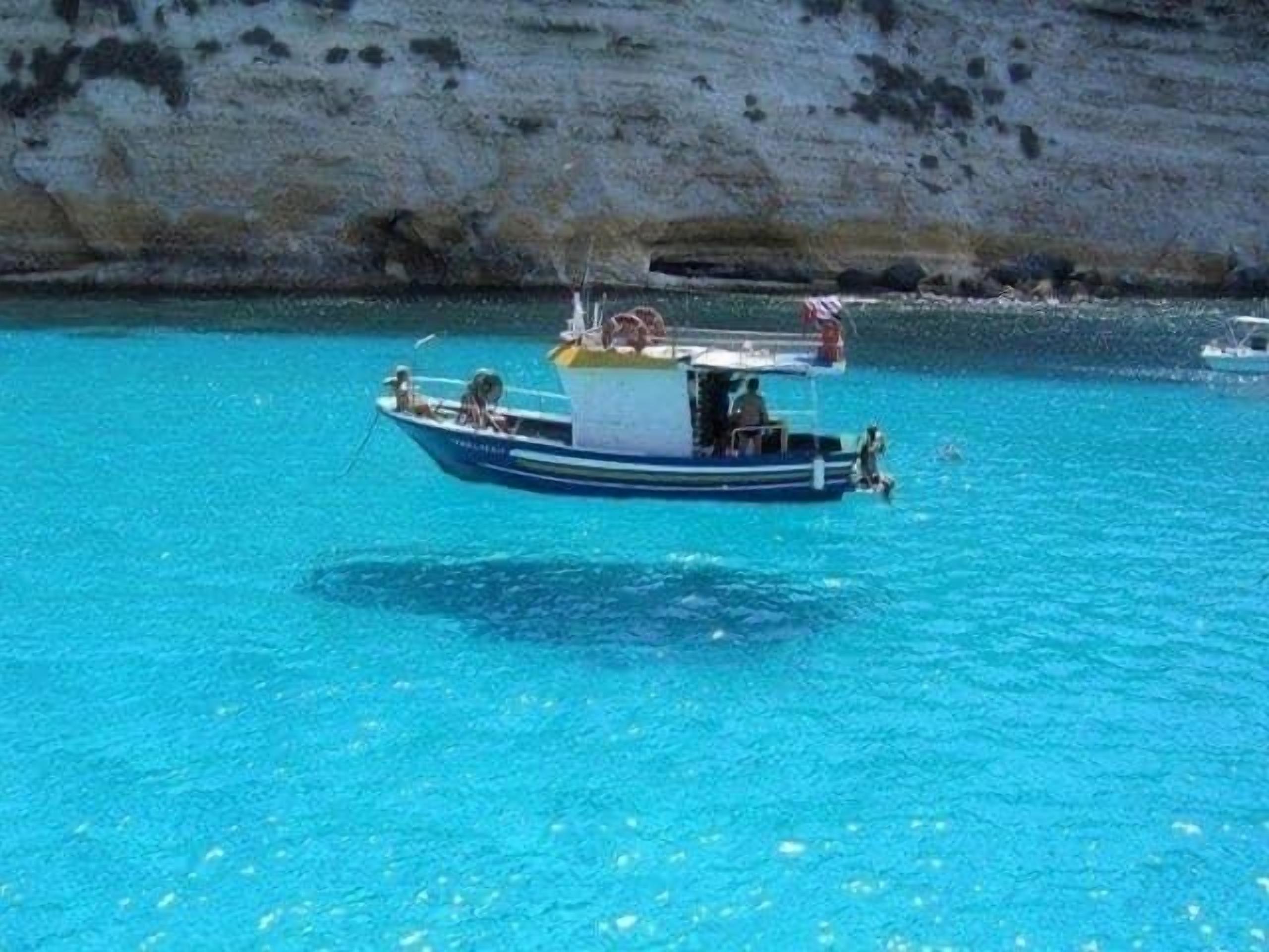 Un bateau sur une eau turquoise et limpide, avec une falaise rocheuse en arrière-plan.