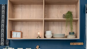 A kitchen with a blue cabinet, a microwave, a toaster, and a wooden shelf with dishes and a clock. - Harbour Terrace 18 (Cape Town)