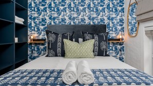 A neatly made bed with rolled towels, a patterned headboard, and a blue and white wall design. - Harbour Terrace 18 (Cape Town)