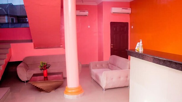 A room with a pink and orange color scheme, featuring a sofa, a chair, a reception desk, and a column. - Omooke Hotel (Ibadan)