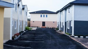 A row of modern buildings with a central structure featuring a beige facade and a black roof. There is a parking lot in front with marked spaces. - Omooke Hotel (Ibadan)