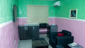 A small, compact room with a kitchenette, a sofa, a coffee table, and a small table with a phone. - Omooke Hotel (Ibadan)
