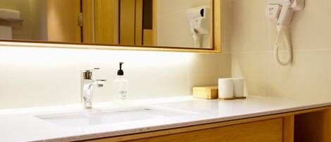 A bathroom with a white sink, a mirror, a hairdryer, and a bottle of shampoo.