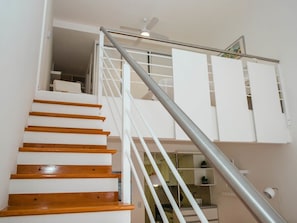 Eine Treppe mit Holzstufen und einem Metallgeländer, die zu einem weißen Raum mit Schränken und einem Deckenventilator führt.