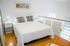 Une chambre à coucher avec un lit, deux tables de chevet, une commode, une fenêtre donnant sur un beau paysage et un tableau accroché au mur.