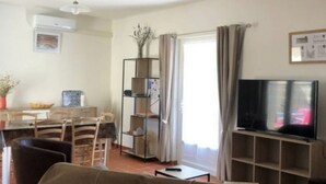 Un salon comprenant un canapé, un téléviseur, une table à manger avec des chaises, une bibliothèque et un ventilateur de plafond.