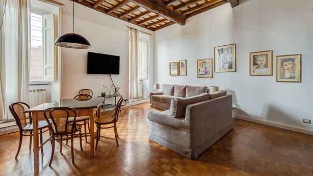 A spacious living room with a wooden ceiling, a grey sofa, a dining table with chairs, and artwork on the walls. - NAVONA ART GALLERY APARTMENT (Roma)