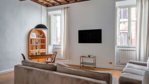 A living room with a sofa, a TV, a bookshelf, and a window with curtains. - NAVONA ART GALLERY APARTMENT (Roma)