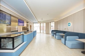 A modern hotel lobby with a reception desk, seating area, and a view of the outdoors.