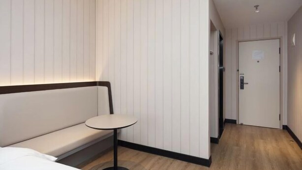 A hotel room with a sofa, a small round table, and a door leading to another room. - HanTing Hotel (Shanghai Jing'an Daning Park) (Shanghai)