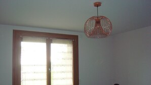 Una habitación con un ventanal grande, un radiador, una cama y una lámpara colgante.