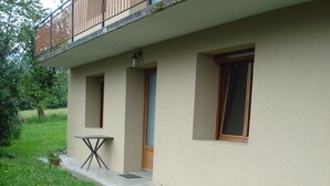 Un edificio con un balcón, una puerta y una ventana. Cerca de la entrada hay una mesa pequeña y plantas en macetas.