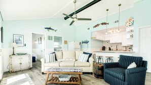 Sala de estar con sofá, sillón y mesa de centro. Zona de cocina con armarios y un refrigerador.