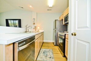 Una cocina moderna con electrodomésticos de acero inoxidable, armarios de madera y encimera blanca.