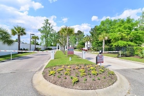 A gated entrance with a no parking sign, a tow away zone sign, and a landscaped area with flowers.