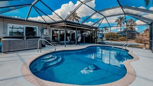 A swimming pool with a hot tub, covered patio, and a view of palm trees.
