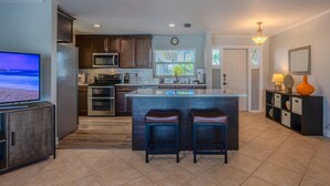 A modern kitchen with dark wood cabinets, stainless steel appliances, a large island with stools, and a television on the left.