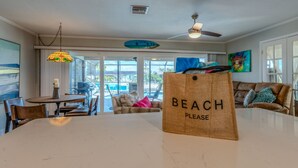 A spacious living area with a dining table, a sofa, and a ceiling fan. A sign on the table reads "BEACH PLEASE".