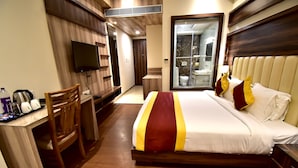 A hotel room with a bed, a desk with a chair, a TV, and a bathroom with a glass shower. - HOTEL CENTELLA  (Gwalior)