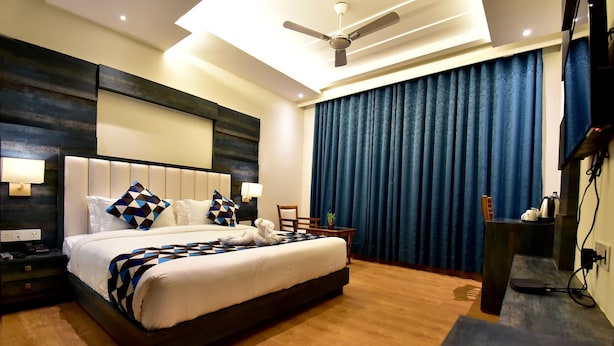 A modern hotel room with a large bed, a ceiling fan, a TV, and a desk with a lamp. - HOTEL CENTELLA  (Gwalior)