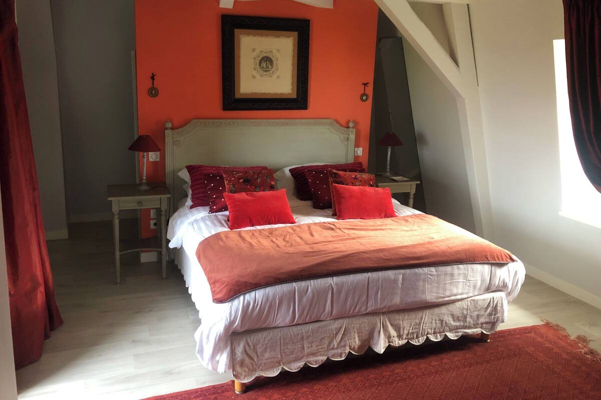 Une chambre à coucher avec un lit, deux tables de chevet, une commode, un tableau encadré au mur et une fenêtre avec des rideaux.