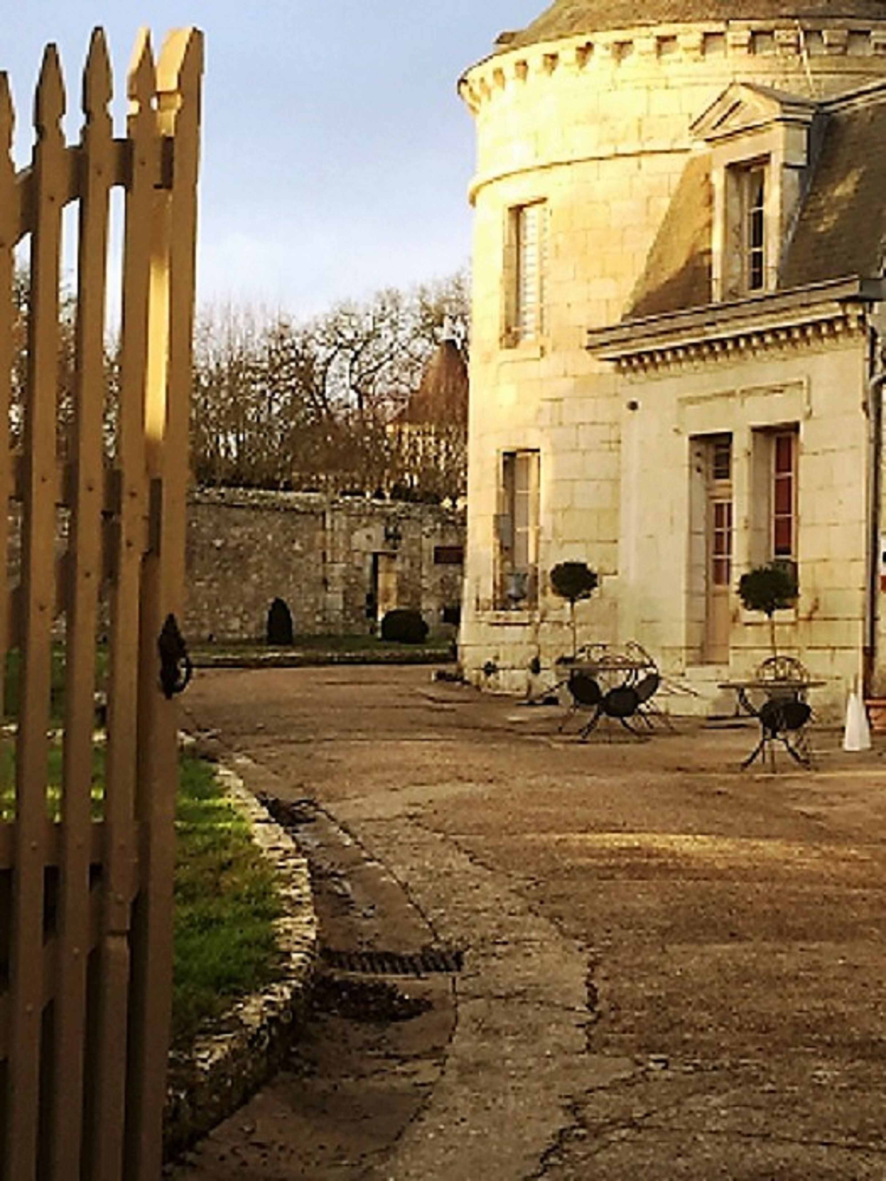 A courtyard with a stone building, a wooden fence, and outdoor seating.