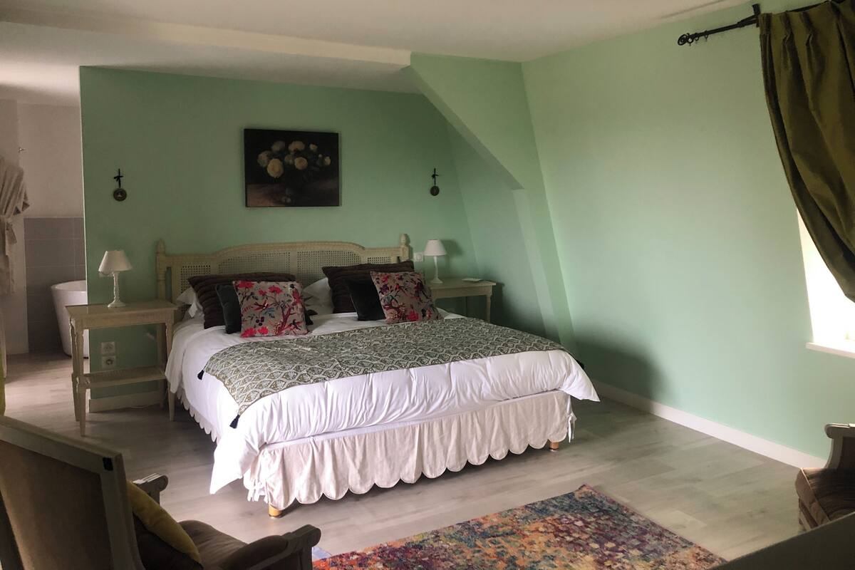 Une chambre à coucher comprenant un lit, deux tables de chevet, une commode, une lampe fixée au mur, une fenêtre avec des rideaux et une lampe sur pied.