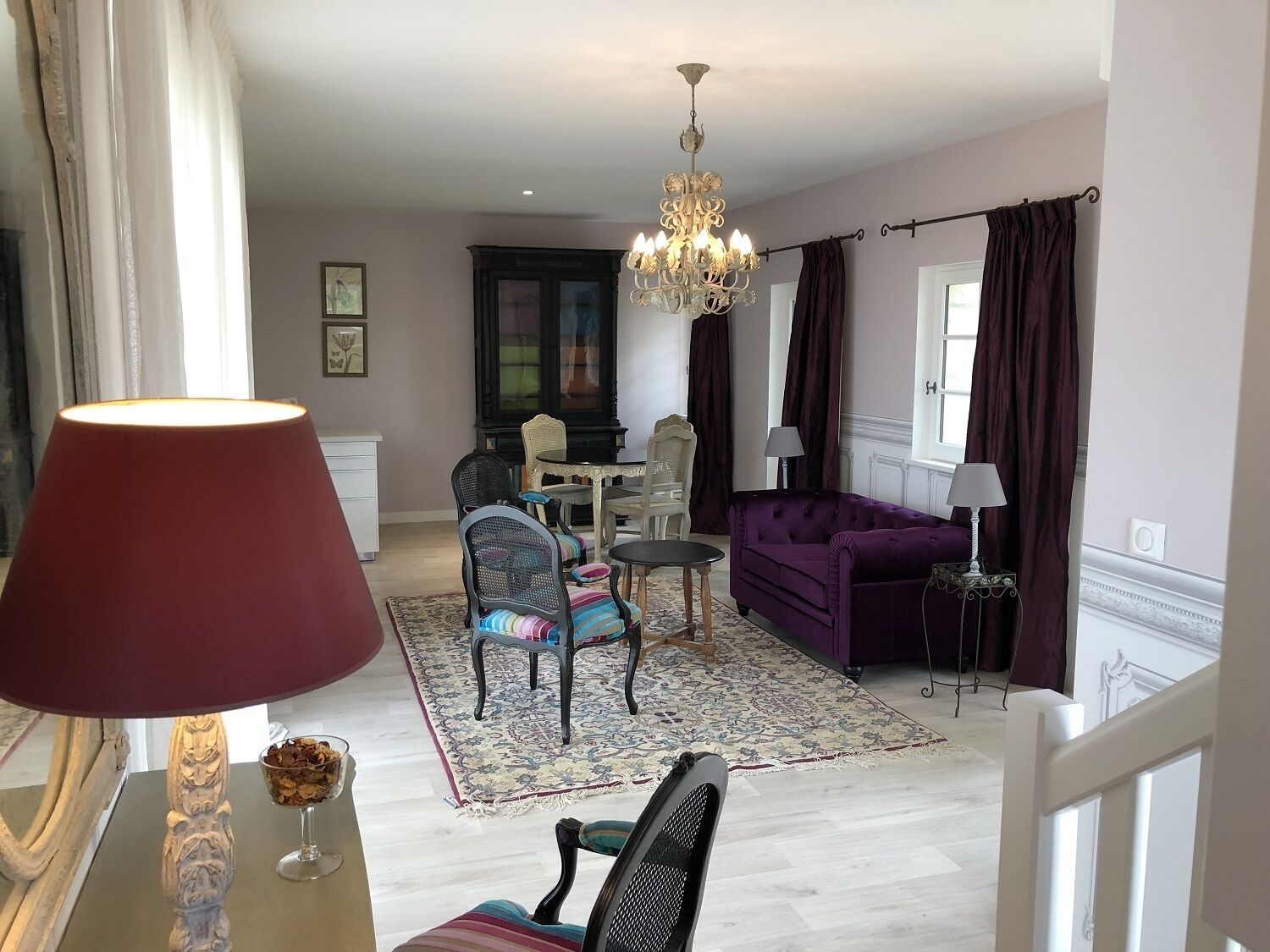Een woonkamer met een kroonluchter, een paarse bank en een eethoek met een tafel en stoelen.