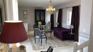 Een woonkamer met een kroonluchter, een paarse bank en een eethoek met een tafel en stoelen.