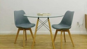 A room with a round glass table and two grey chairs with wooden legs. There are two framed pictures on the wall. - House Valencia 1 (Flores)